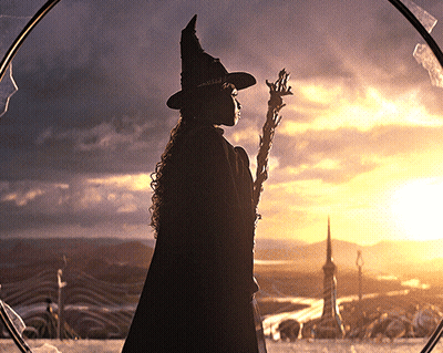 Silhouette Of Woman In Witch Hat Holding Wand In Front Of Sunset GIF