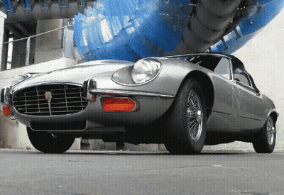 Silver Sports Car Parked In Front Of Blue Sculpture GIF