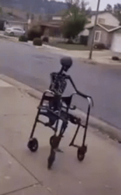 Skeleton Sitting on Walker on Sidewalk
