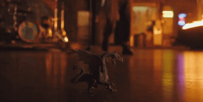 Small Toy Dragon Sitting On Wooden Floor In Dark Room GIF