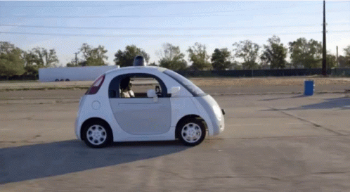 Small White Car Driving Next To Blue Barrel GIF