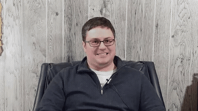Smiling Man In Glasses Sitting In Chair GIF