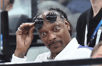 Snoop Dogg Adjusts His Sunglasses While Sitting In A Stadium GIF
