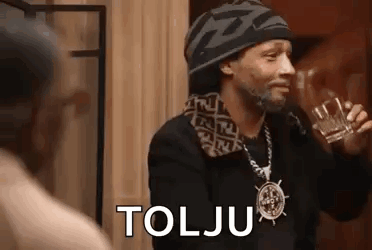 Snoop Dogg Is Drinking A Glass Of Whiskey While Wearing A Hat And Necklace . GIF