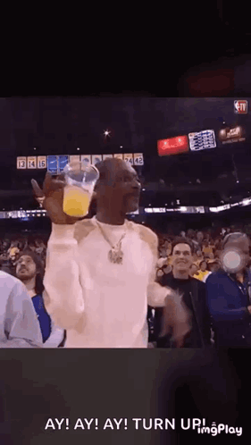 Snoop Dogg Is Holding A Cup Of Orange Juice In Front Of A Crowd Of People At A Basketball Game . GIF