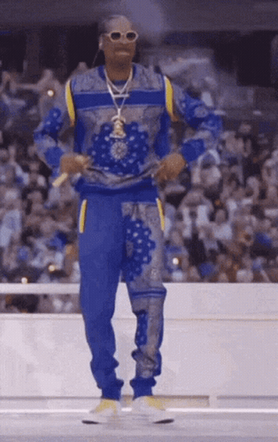 Snoop Dogg Is Standing In Front Of A Crowd Wearing A Blue And Yellow Outfit . GIF