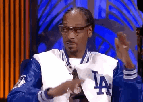 Snoop Dogg Is Wearing A La Dodgers Jacket And Glasses While Talking On A Stage . GIF