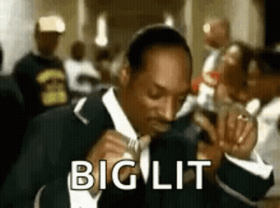Snoop Dogg Is Wearing A Suit And Tie And Singing Into A Microphone In A Crowded Room . GIF