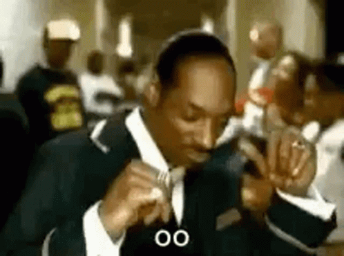 Snoop Dogg Is Wearing A Suit And Tie And Smoking A Cigarette In A Crowded Room . GIF