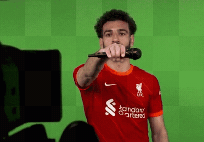 Soccer Player In Red Shirt Holding Microphone Pointing At Camera GIF