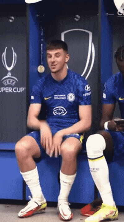 Soccer Player Sitting On Bench In Locker Room In Front Of UEFA Super Cup Sign GIF