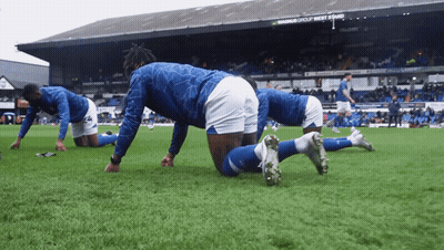Soccer Players Stretching On The Field In Front Of A Sign That Says Magnus Group West End GIF
