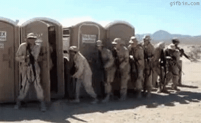 Soldiers Standing In Front Of Portable Toilets In Desert GIF