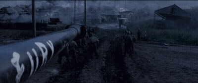 Soldiers Walking Down Dirt Road Past Building Saying A GIF