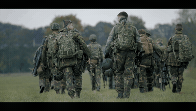 Soldiers Walking In Field, One With Helmet GIF