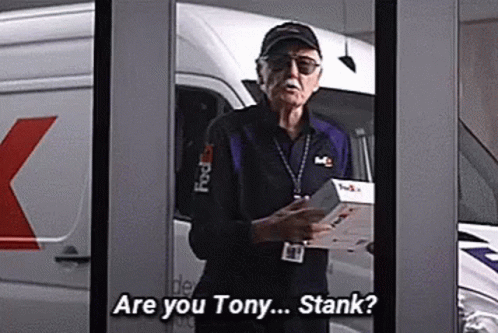 Stan Lee Is Standing In Front Of A Fedex Van Holding A Box And Talking To Someone . GIF