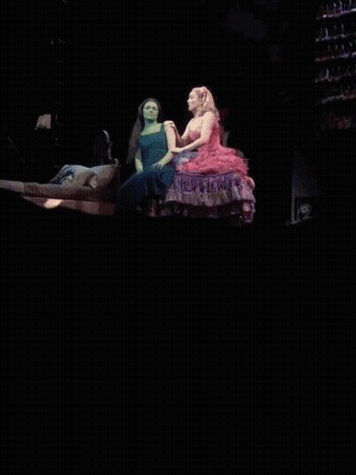 Standing Woman In Pink Dress Next To Sitting Woman On Bed GIF
