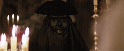 Statue Of Man In Black Mask And Hat In Front Of Candles GIF