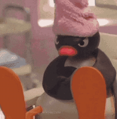 Stuffed Penguin In Pink Hat Sitting On Toilet GIF
