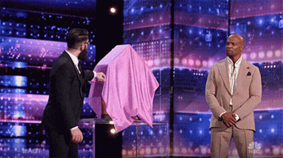 Suited Man Holds Pink Cloth Over Another's Head GIF