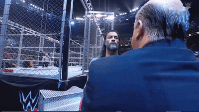 Suited Man Talking In Wrestling Ring W Logo GIF