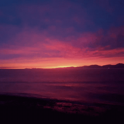 Sunset Over The Ocean With Mountains In The Background GIF