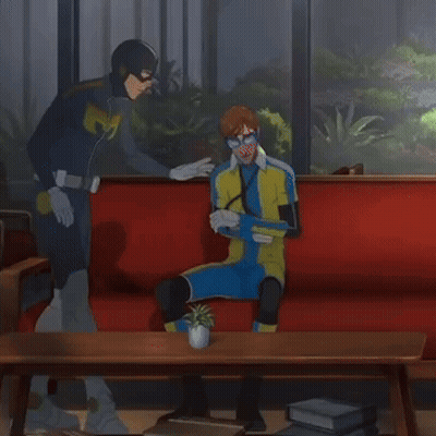 Superhero Man And Another Man On Red Couch GIF