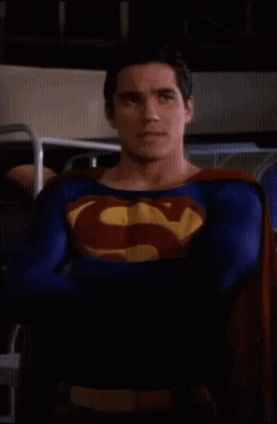 Superman Costume Man Standing With Arms Crossed In Dark Room GIF