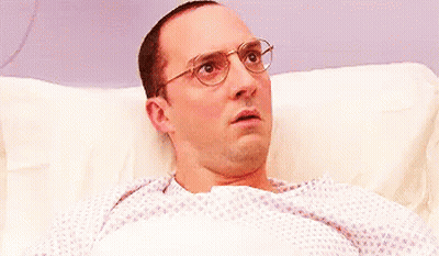 Surprised Man With Glasses Lying In Hospital Bed GIF