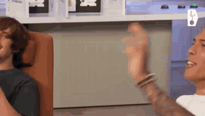 Tattooed Man Sitting While Another Throws Ball GIF