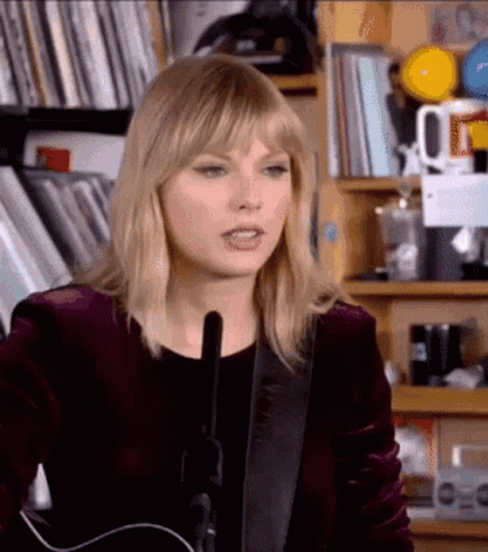 Taylor Swift Is Playing A Guitar In Front Of A Microphone In A Room . GIF
