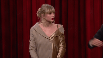 Taylor Swift Is Standing In Front Of A Red Curtain With A Man In A Suit . GIF