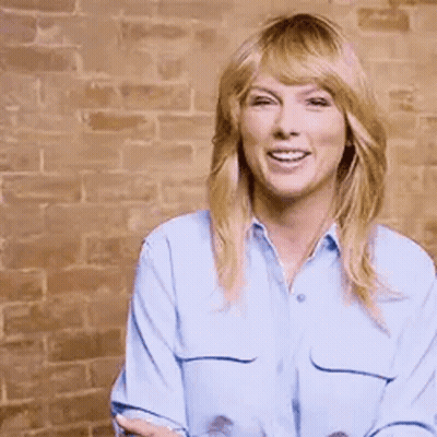 Taylor Swift Smiling In Front Of Brick Wall GIF