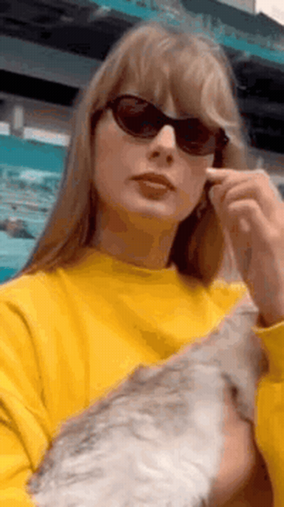 Taylor Swift Wearing Sunglasses And Yellow Sweater Holding Cat GIF