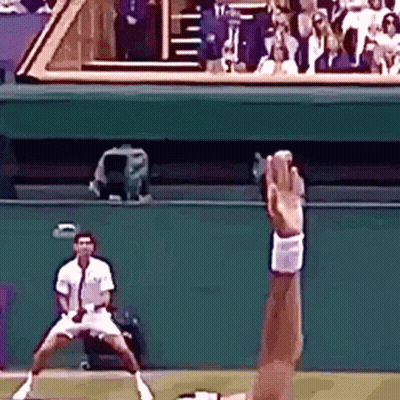 Tennis Player Reaching For Ball While Another Watches GIF