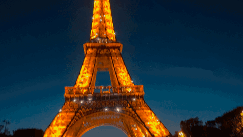The Eiffel Tower Is Lit Up At Night Against A Dark Blue Sky GIF