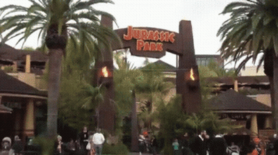 The Entrance To Jurassic Park Is Shown With Palm Trees In The Background GIF
