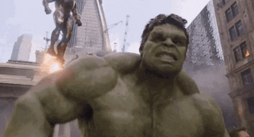 The Hulk Is Standing In The Middle Of A City With A Statue In The Background . GIF