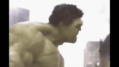 the hulk is without a shirt and is standing in front of a building .