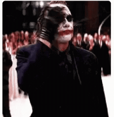 The Joker Is Holding A Gun In His Hand And Pointing It At The Camera . GIF