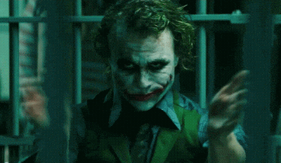 The Joker Is Holding A Knife In His Hand In A Dark Room . GIF