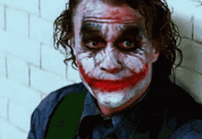 The Joker Is Leaning Against A Wall With His Face Painted And Making A Funny Face . GIF