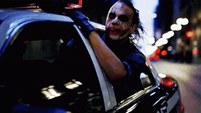 The Joker Is Sitting In The Back Of A Police Car And Looking Out The Window . GIF