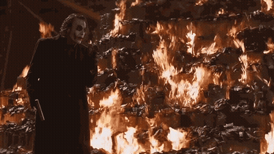 The Joker Is Standing In Front Of A Large Pile Of Burning Papers . GIF