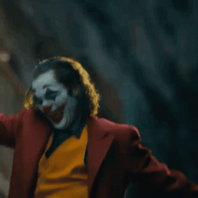 The Joker Is Standing On A Set Of Stairs With His Arms Outstretched . GIF