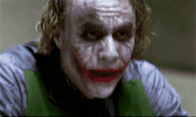 The Joker Is Wearing A Green Vest And A Gray Shirt And Has A Funny Face On His Face . GIF