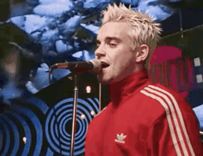 The Man Is Wearing A Red Adidas Jacket And Singing Into A Microphone . GIF