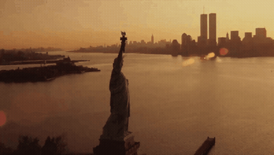 The Statue Of Liberty Is In The Foreground And The Twin Towers In The Background GIF