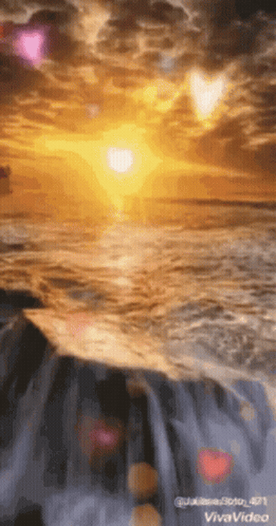 The Sun Is Setting Over The Ocean And A Waterfall Is In The Foreground . GIF