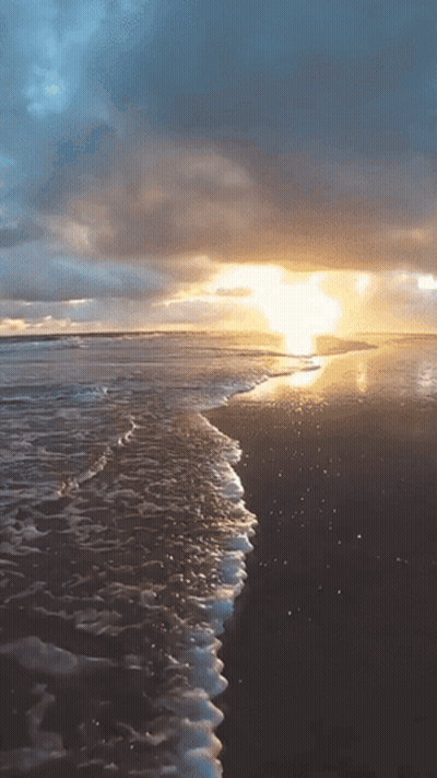 The Sun Is Setting Over The Ocean And The Waves Are Crashing On The Beach GIF